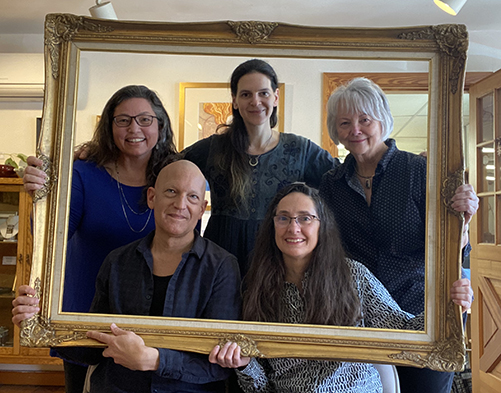 four women and one man in gallery holding a big frame